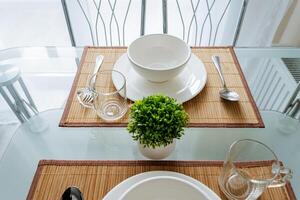 A wellarranged dining table with plates, bowls, forks, and knives, plus a vibrant green plant, creates a warm, inviting, and visually appealing atmosphere for a pleasant dining experience photo