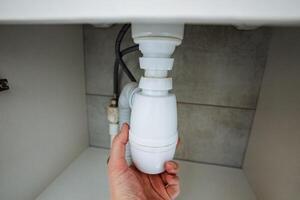 A person is meticulously securing a drain pipe beneath a sink, ensuring that it remains firmly in position and operates efficiently, especially during necessary plumbing maintenance tasks photo