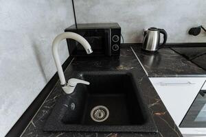 The image features a sleek kitchen sink with a modern faucet in the foreground, while a practical microwave in the background enhances the kitchens utility and aesthetics photo
