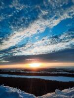 As the day comes to a close, the sun is gracefully setting over a pristine, snowy landscape, painting the sky with beautiful hues of orange and pink, creating a serene winter scene photo