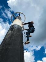 A determined individual, brimming with enthusiasm, skillfully climbs a tall pole with a sturdy ladder, embracing the adventure and courageously facing the challenges of the structure photo