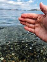 A hand is gently reaching out toward the calm surface of a lovely body of water, inviting a connection with the soothing element, as nature surrounds the scene beautifully photo