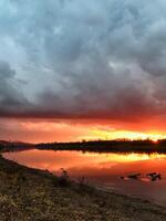 The breathtaking view of a colorful sunset casting its vibrant hues over a serene lake, complemented by a beautifully textured cloudy sky, creates a perfect natural scene of tranquility photo