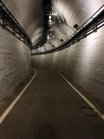 A deserted tunnel stretches ahead, featuring a distinctive white line running alongside it, creating a stark contrast against the grey and dark surroundings, bathed in monochrome tones photo