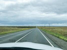 A car is smoothly driving along a picturesque countryside road on a moderately cloudy day, relishing the beautiful views of nature while skillfully navigating the wellpaved path ahead photo