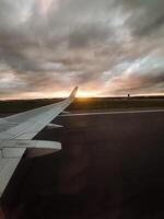 A magnificent airplane wing gracefully glides over the airport runway as the sun sets, with an array of vibrant hues painting a strikingly beautiful dusk sky filled with color photo