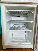 The interior space of a completely empty refrigerator is prominently visible, with the appliances door standing wide open, revealing only its vacant shelves and compartments located inside photo