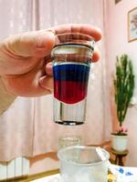 At this moment, an individual is holding a small shot glass that is filled with a striking and vibrant mix of red and blue liquid, illustrating a oneofakind and colorful drink design photo