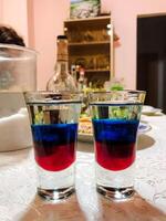 A beautifully arranged table in a bright room features two elegant shot glasses with vibrant red and blue liquids, creating a captivating visual display for drink lovers photo
