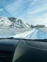 A car is steadily driving along a snowy road, navigating through the frostcovered landscape while the windscreen wipers clear the glass, preparing for an adventurous winter journey photo