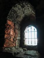 A weathered stone wall features a barred window, highlighting its ancient structure and the impact of time. This site evokes a sense of history, echoing stories of the past photo