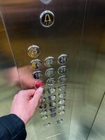 A person is intently pressing a bright red button located inside an elevator while they are waiting for it to take them to their desired floor, surrounded by silver panels photo
