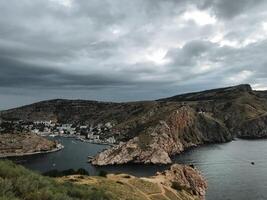 This describes a breathtaking view showcasing a serene body of water that is beautifully surrounded by majestic mountains, all set against a backdrop of clouds on a cloudy day photo