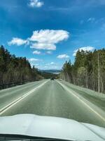 A car is steadily driving down a long stretch of highway, flanked by lush trees on both sides, creating a picturesque scene that showcases the beauty of nature along the road photo