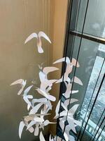 A colorful bunch of delicate paper birds is gracefully hanging from a thin string right in front of a window, creating a beautiful and whimsical display of art and design photo