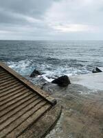 A beautifully crafted wooden staircase ascends toward the vast ocean on a cloudy day, where the sky meets the water, creating a serene yet moody atmosphere and captivating visual photo