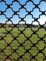 This is a picturesque view showcasing a sprawling field, beautifully framed by an intricately designed wrought iron fence, allowing us to appreciate the scenery beyond it photo