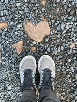 A person is standing beside a beautifully shaped heart rock that is resting on the ground, creating a picturesque scene perfect for snapping photos and enjoying natures artistry