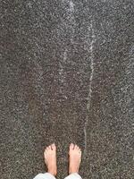 A persons feet are standing on a wet concrete surface that has recently been poured, showcasing the texture and dark sheen of the freshly mixed concrete underneath them photo