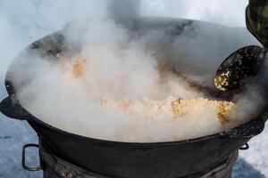 A person is actively cooking food in a large pot, and there is visible smoke wafting out from it, indicating that something is being prepared, likely on a stove over a flame photo