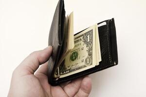A charcoal-hued money pouch containing American banknotes on a white surface.A wallet with money. photo