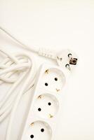 A white three-outlet surge protector with a pale cord on a minimalist white backdrop. photo