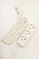 A three-way extension cable with a pearl-white wire and sockets on a white setting. photo
