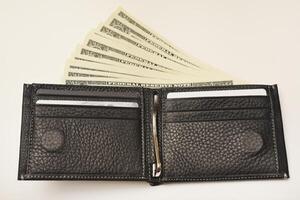 A black zippered wallet with cash inside, set against a white surface. photo