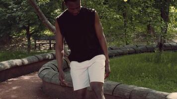 A young African American man engages in a fitness routine at a public park. He walks along a winding path, surrounded by trees and greenery, embracing a healthy lifestyle. video