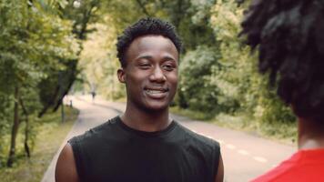 A young African American man smiles as he enjoys his workout in a public park. Surrounded by greenery, he embodies a healthy, active lifestyle amidst nature. video