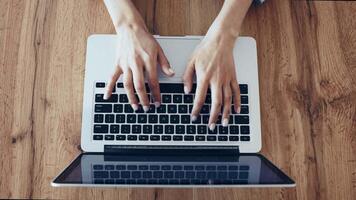 Hands are actively typing on a laptop positioned on a wooden surface. The natural light enhances the workspace atmosphere, suggesting productivity and concentration. video