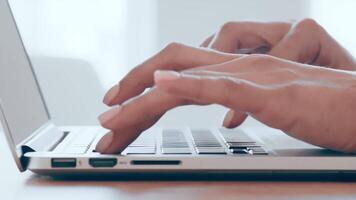 A person is focused on typing on a laptop keyboard while seated at a wooden desk. The soft daylight illuminates the workspace, creating a serene atmosphere for work. video