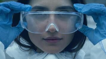 A young Middle Eastern woman adjusts her protective eyewear while preparing for a science experiment in an outdoor urban environment. She exudes confidence and curiosity as she embraces the project. video