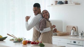 A smiling couple joyfully prepares meals in a sunlit kitchen. Fresh vegetables and cooking utensils are spread across the counter as they share a fun moment while cooking. video