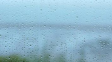 Raindrops on a glass window create a blurred view of a serene landscape during a rainy day video