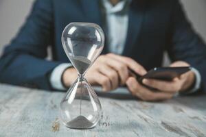 A man in a suit is using his phone while holding an hourglass photo