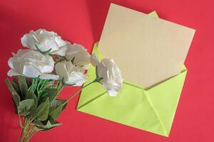 An envelope with white roses and a green envelope on a red background photo