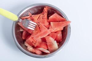 Freshly cut watermelon slices in a stainless steel colander with fork photo