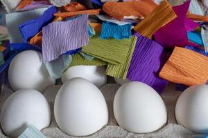 White eggs in a carton surrounded by colorful pieces of paper. photo