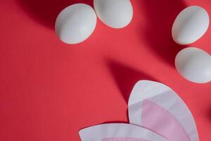 A red background with white eggs and a paper cut out of a bunny photo