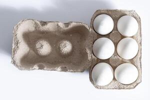 Cardboard box with six white eggs on a bright white background photo