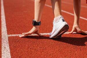 Female athlete at the starting line on a running track, preparing for a sprint, focused and determined for race competition and peak performance. photo