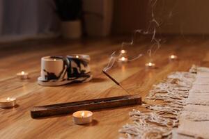 Close-up of burning incense stick with candles on wooden floor, creating a calm, meditative atmosphere for yoga, relaxation, or mindfulness practices. Warm, cozy, and peaceful setting. photo
