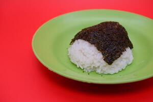 Rice Topped with Dried Nori Seaweed on a Green Plate, Isolated on Red Background photo