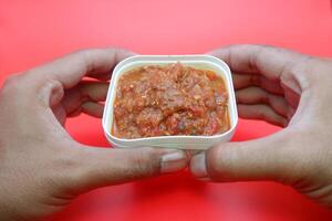 Homemade Lamongan Sambal in a Square White Container with a Deep Red Background photo