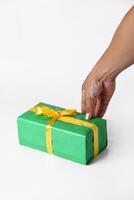 Hand Unwrapping a Green Gift Box with a Yellow Ribbon on White Background photo
