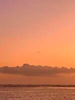 golden sunset over Kelan Beach, Bali, with calm ocean waves and a scenic breakwater. A tranquil coastal scene with warm hues serene atmosphere. photo