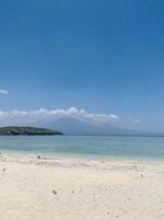 Menjangan Island, West Bali, with crystal-clear blue waters and pristine white sands. Three majestic mountains in the distance frame the panorama, creating a serene natural atmosphere. photo