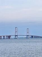 Suramadu Bridge Over Madura Strait with Calm Ocean and Blue Sky Longest Cable-Stayed Bridge in Indonesia, Coastal View, Urban Skyline, Maritime Landmark, Travel Destination, Tourism, Architecture. photo