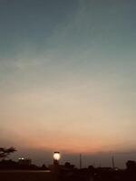 A cozy cafe corner with a vintage lamp casting soft glow as twilight paints the sky in warm orange, pale blue. Distant towers silhouette against dusky sky, adding a tranquil depth. photo